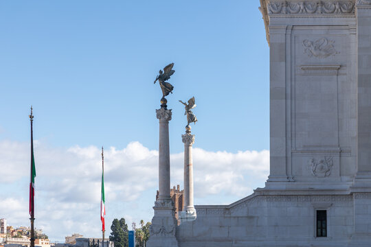 View of the bronze winged Victory statues atop columns at the Altar of the Fatherland with Italian flags against a clear blue sky in Rome, Lazio, Italy.