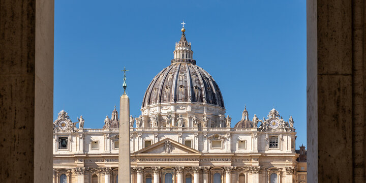 View of the dome of St. Peter's Basilica framed by architectural columns under a clear blue sky in Vatican City, Vatican City.