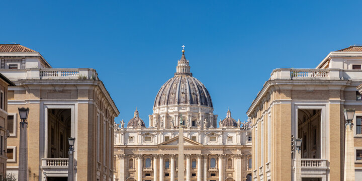View of St. Peter's Basilica dome framed by classical buildings under a clear blue sky in Vatican City, Vatican City.