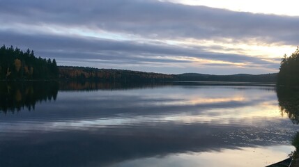 Fototapeta premium Calm lake reflecting autumn forest and cloudy sky at dusk