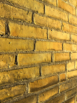 Perspective view along a wall of golden colored painted bricks lit by morning sun
