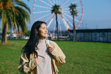 Fototapeta premium Woman with backpack enjoying a sunny park day, a ferris wheel in the background, casual jacket, breeze in hair, relaxed mood, travel vibe, outdoor leisure and exploration