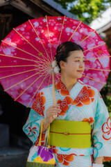 A young Japanese woman in a colorful traditional yukata holding a pink cherry blossom parasol at Senso-ji Temple in Tokyo, Japan. © Zenstratus