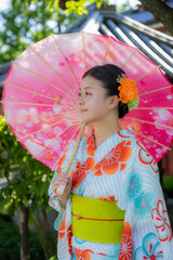 A young Japanese woman wearing a colorful floral yukata holds a cherry blossom parasol in a traditional garden in Senso-ji Temple, Tokyo, Japan, showcasing culture. © Zenstratus