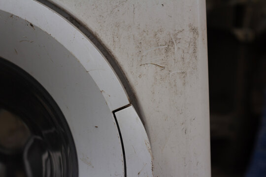 Close up photo. Old dirty white washing machine with stains and scratches on body and round door frame. Household hardware detail. Appliance in city junk yard. Clean, rent, wash, dry, trash, garbage