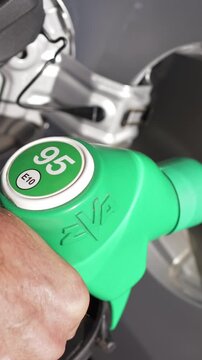 Vertical screen. Hand grips green fuel nozzle labeled 95 E10 as it is inserted into the car's fuel tank at a gas station, highlighting the refueling process