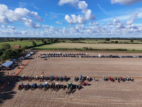 Covehithe, England, United Kingdom - 05 October 2026: Aerial view of vintage tractors parked in a large agricultural field with rows of cars and a blue sky.