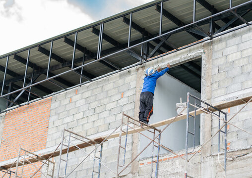 Construction builder leveling and plastering the top edge of a window opening on a concrete block wall at a building site.