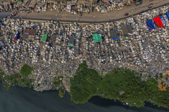 Dhaka, Bangladesh - 04 October 2026: Aerial view of Kamrangirchar showing dense clusters of plastic waste bags, makeshift shelters, and polluted riverbanks with lush vegetation.