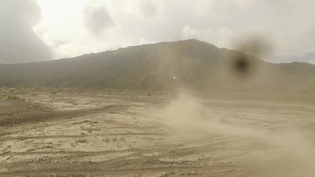 Motocross Rider Kicking Up Dust Cloud on Off-Road Dirt Bike Adventure in Volcanic Desert Landscape at Bromo, East Java, Indonesia