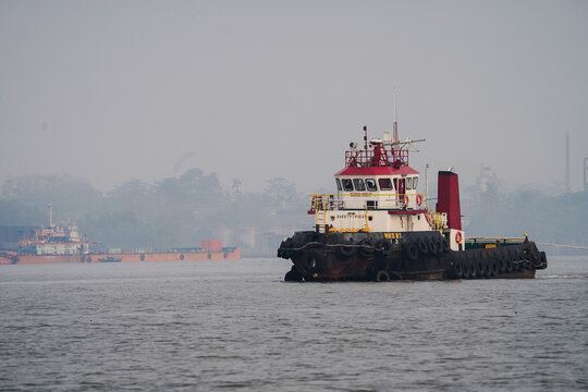 Industrial maritime tugboat vessel sailing on calm river water under a foggy morning sky for transportation and logistics operations
