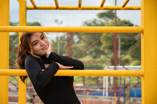 Colombian teen girl posing confidently on yellow monkey bars at an outdoor park, embracing youth and a cheerful lifestyle in a vibrant, natural setting