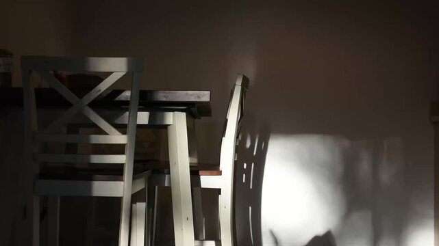 White dining chairs and table casting dramatic shadows on wall in dimly lit room