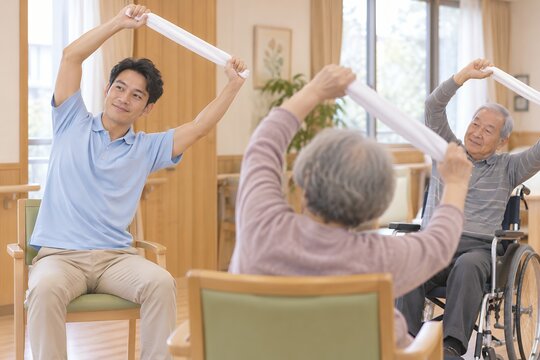 介護施設で椅子と車椅子に座った高齢者が外国人材の男性職員とタオル体操を行う