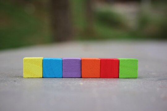 Six small cubes arranged in a row on a surface with a softly blurred outdoor background, creating a versatile creative concept with copy space for text and various design needs.
