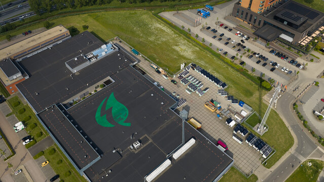 Duiven, Netherlands - 16 June 2026: Aerial view of the Volta Energy facility featuring a large green logo on the flat roof, rows of solar panels, and an adjacent parking lot.