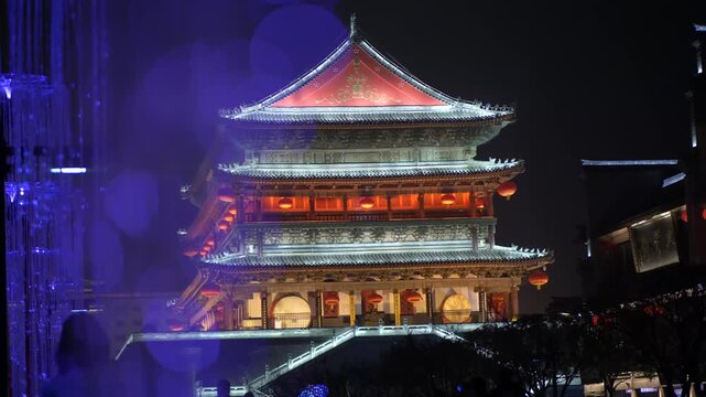 Illuminated traditional Chinese bell tower at night with red lanterns and golden roof in Xi'an city center