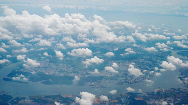 Aerial View of City and River Through Fluffy Clouds from Airplane Window