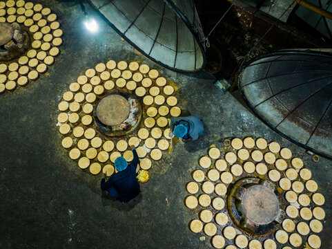 Bogura, Rajshahi Division, Bangladesh - 14 December 2024: Aerial view of workers in a jaggery factory with circular molds arranged in patterns on the floor and large metal covers.