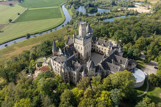 Pattensen, Germany - 17 September 2026: Aerial view of Marienburg Castle, a historic neo-Gothic palace surrounded by lush forests, green fields, and a winding river.