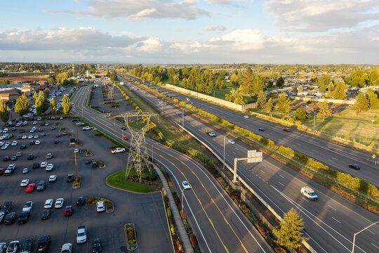 Woodburn, Oregon, United States - 25 September 2026: Aerial view of Interstate 5 highway with traffic and an adjacent parking lot surrounded by trees and suburban landscape.