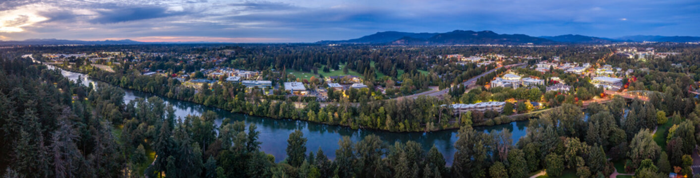 Eugene, United States - 26 September 2026: Aerial view of the Willamette River flowing through Eugene, Oregon, surrounded by lush trees, residential areas, and distant mountains under a twilight sky.