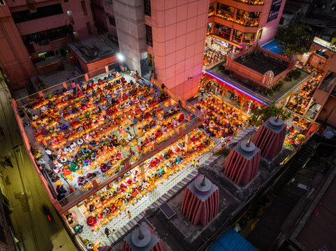 Dhaka, Bangladesh - 11 November 2023: Aerial view of Swamibagh Temple, with many people gathered on the rooftop terrace, illuminated by numerous glowing candles during a religious festival.