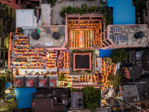 Dhaka, Bangladesh - 11 November 2023: Aerial view of Swamibagh ISKCON Temple with devotees holding lit lamps during a festival in the courtyard, surrounded by urban rooftops.