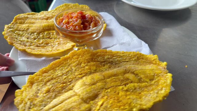 waiter holding plate of crispy fried patacones with salsa in restaurant
