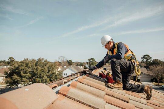 Professional roofer in safety gear working on a residential tile roof during a sunny day