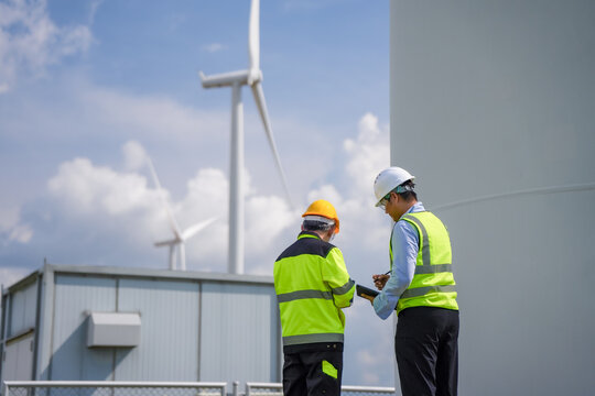 Wind turbine engineer technician renewable energy safety vest hard hat wind farm clean energy worker industrial facility remote collaboration discussing maintenance plan outdoors blue sky with