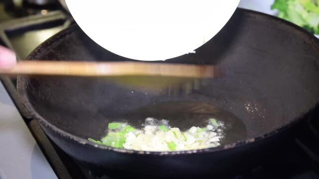 Saut&eacute;ing chopped garlic and green onions in a seasoned wok with hot oil on a gas stove
