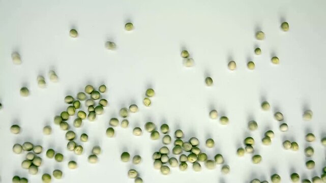 Green peas scattering across a white surface in slow motion