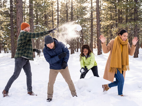 Four diverse friends playing a snowball fight for playful winter friendship outdoors