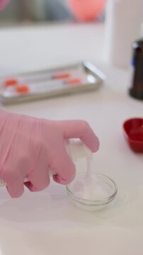 Vertical video. Squeezing gel. Skin care. Unrecognizable female hands in pink gloves product into glass bowl beautician for cosmetic procedure in salon.