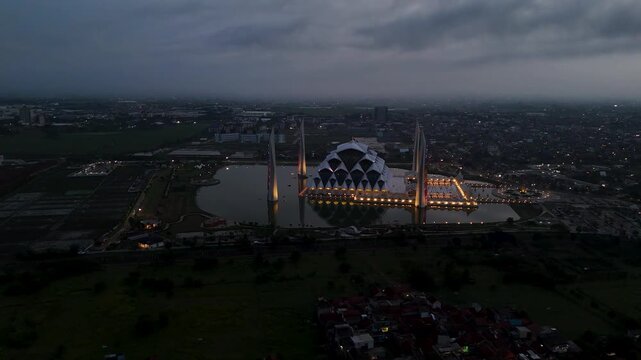 Aerial view of the illuminated Al Jabbar Grand Mosque reflecting in the surrounding water at dusk in Bandung, West Java, Indonesia.