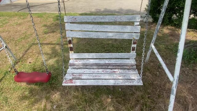 Old and weathered wooden swing bench with peeling paint in an abandoned garden