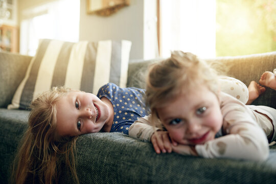 Portrait, siblings and children on break, lounge and girls with smile on sofa, bonding and together. Happy, sisters and relax on couch, home and kids in living room, chill or family in apartment