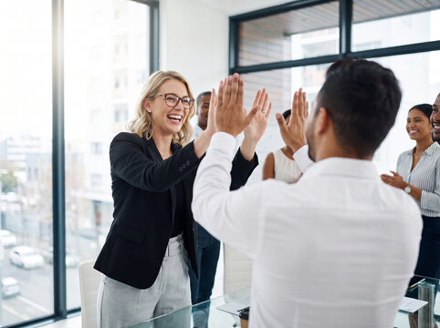 Happy business colleagues celebrating success with a high-five in a modern office environment.