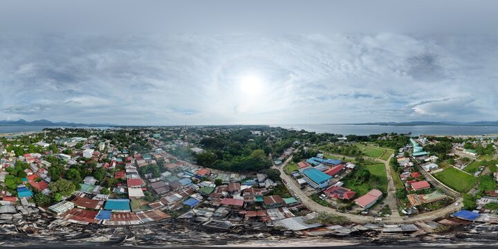 360 aerial panorama over Barangay Masipag, Puerto Princesa, Palawan: burned houses amid dense tin roofs, with port, storage tanks, cemetery, bay and mountains.