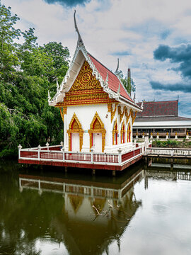 Beautiful traditional Thai temple ordination hall floating on a pond with water reflection