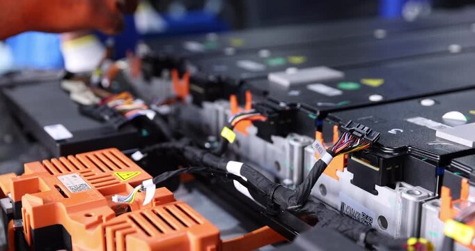 Close-up of a technician wearing orange gloves handling multipin wiring harness connectors inside an electric vehicle battery pack.