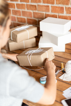 Person wrapping gifts with brown paper and white string on a table.