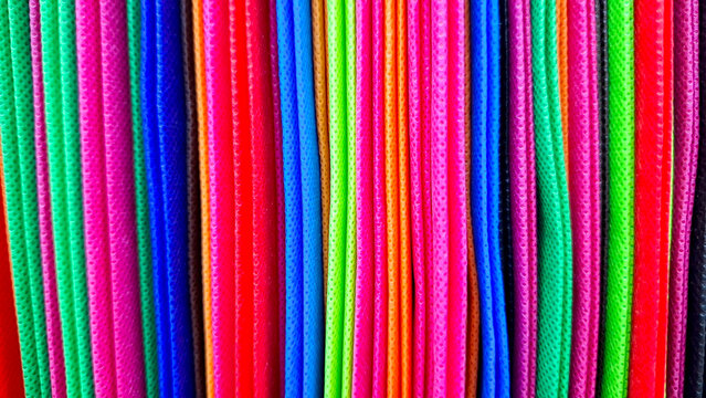 Vertical close-up shot of stacked vibrant colorful non-woven fabric shopping tote bags. Eco-friendly reusable spunbond polypropylene bag texture background for retail store.