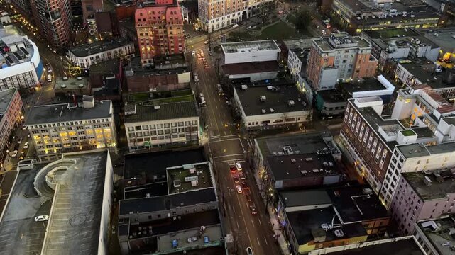 Aerial view looking down on a downtown Vancouver street with cars, intersections and rooftops at dusk, an urban grid of older buildings in the evening.