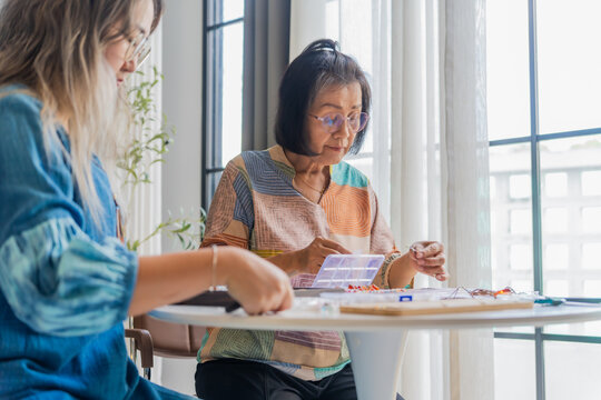 Two Asian woman making handcrafted jewelry together at home