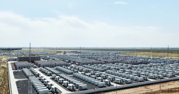 Low aerial video over neat rows of white battery storage containers in a fenced station in arid sandy land, the world's largest operational energy storage power station in Dengkou county, China