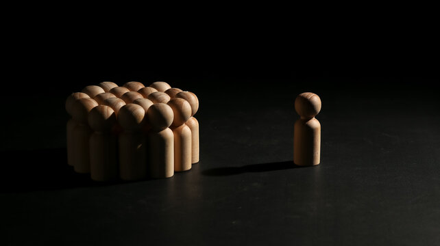 Single wooden peg doll standing apart from a large crowd, representing individuality, social exclusion, standing out from the crowd, loneliness, and leadership.