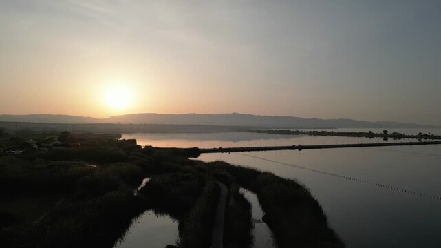 Aerial view of the historic Saline Conti Vecchi salt pans at sunset with calm water and surrounding reeds in Assemini, Sardegna, Italy.