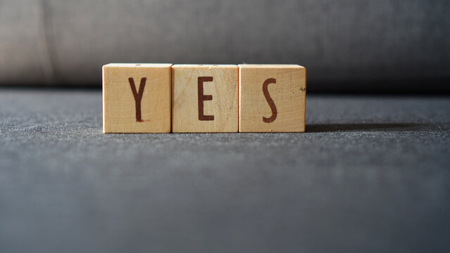 the word "YES" made of arranged wooden cubes, isolated on a dark grey background